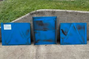1b - Dupont Welder Services Three blue metal utility boxes placed in a row on a concrete surface with a grassy area behind.