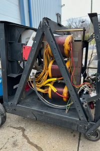 Three large yellow-coiled transformers on a metal frame with red and black cables, outdoor industrial setup.