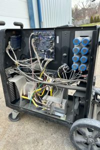 Open portable electrical control cabinet on a wheeled cart, showing a circuit board, wiring, a transformer, and blue terminal blocks on the right.