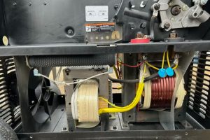 6a - Dupont Welder Services Interior view of industrial equipment showing two large coil assemblies (transformers) with yellow and red wires, a cooling fan, and metal framing with a warning label on the top panel.