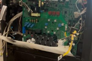 Interior view of an opened electronic device showing a green circuit board, ribbon cables, and assorted wiring connected to components.