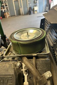 Circular green foam air filter mounted on top of a small engine in a garage or workshop set-up, awaiting maintenance